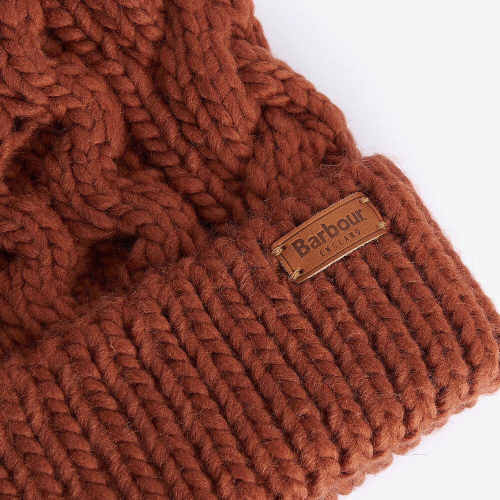 Barbour PENSHAW Womens Pom-Pom Beanie Warm Ginger close-up detail view showing cable-knit structure and logo-embossed leather badge.
