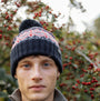 Barbour CASE FAIRISLE Mens Bobble Beanie Blue Granite front view worn by a model with berries in the background.