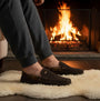 Barbour MONTY Mens Slippers Brown side view worn by a person near a fireplace on a soft rug.