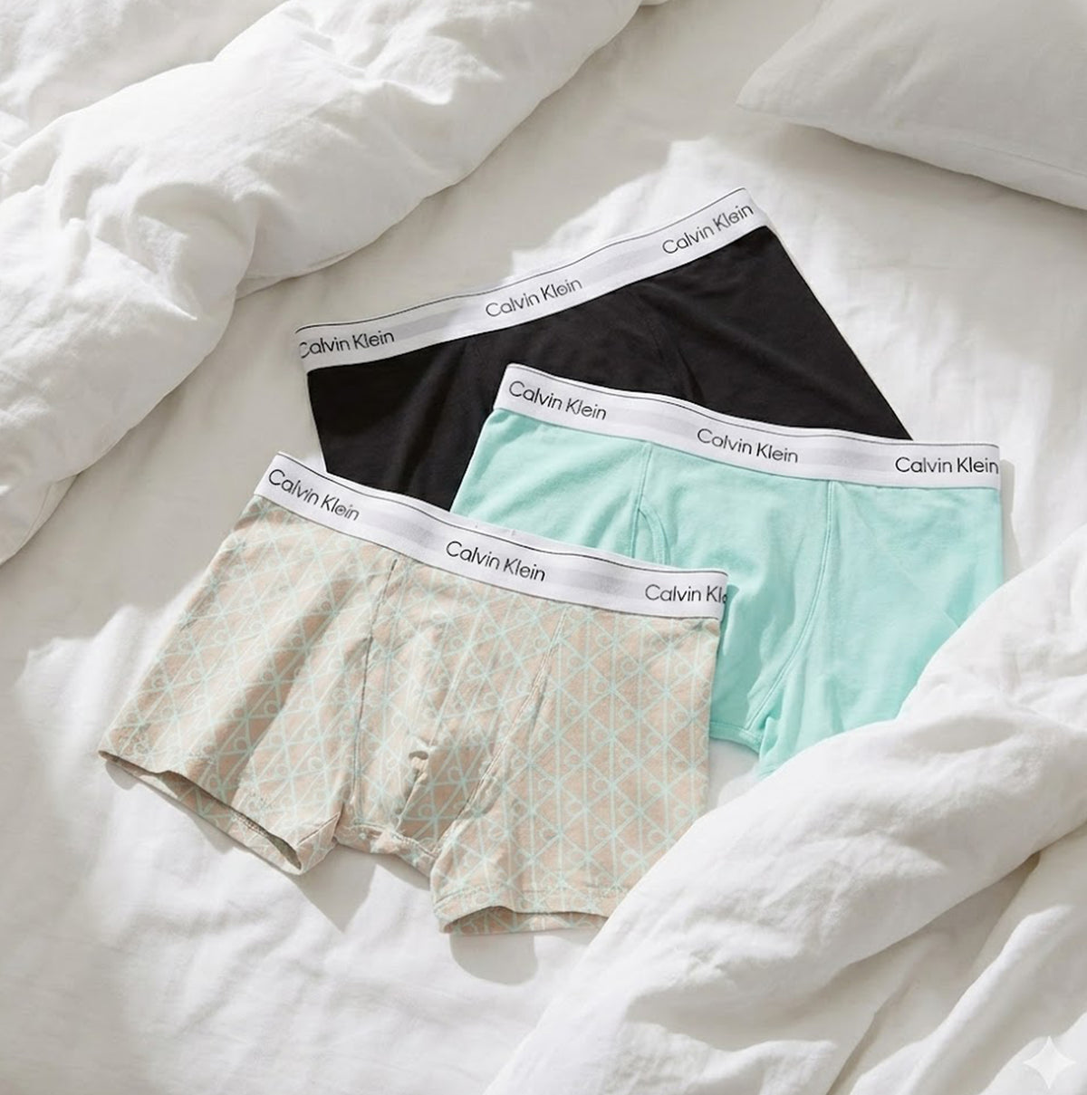 Calvin Klein COTTON BLEND Mens 3 Pack Trunks Multicoloured displayed on a bed, featuring black, mint, and patterned trunks.